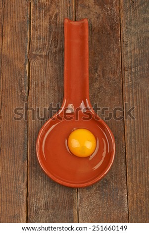 Raw eggs in a clay spoon on wooden table