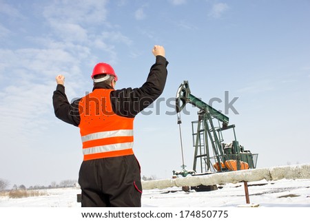 worker on an oil pump with his back holding raised hands,best focus on the helmet and vest