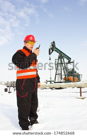 Oil Industry Pump jack with one oil worker who using a portable radio.,best focus on the helmet and vest, soft focus pump
