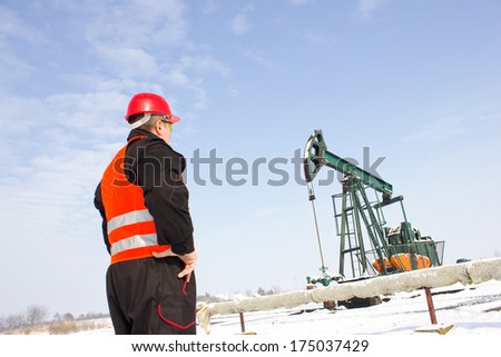 Oil Industry Pump jack with one oil worker holding a hand-held radio,best focus on helmets, vests, pump soft focus