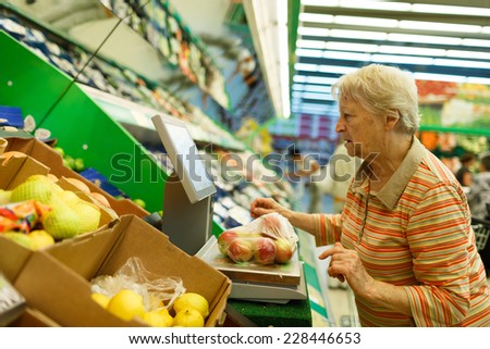 Elderly woman weighing goods on digital weight in supermarket, shopping for fruits and vegetables in produce department of a grocery store/supermarket ( color toned image )