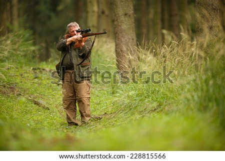 hunter with his rifle in spring forest, hunter holding a rifle and waiting for prey, hunter aiming and shooting