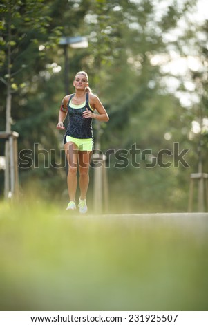 Young lady running. Woman runner running through the spring park road. Workout in a Park. Beautiful fit Girl. Fitness model outdoors. Weight Loss. Golden hour.