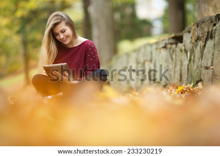 Young woman using tablet outdoor sitting on grass and smiling. Girl using digital tablet pc in the park. Student using tablet after school.