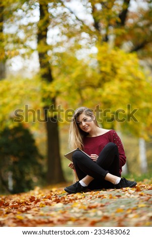 Young woman using tablet outdoor sitting on grass and smiling. Girl using digital tablet pc in the park. Student using tablet and laughing.