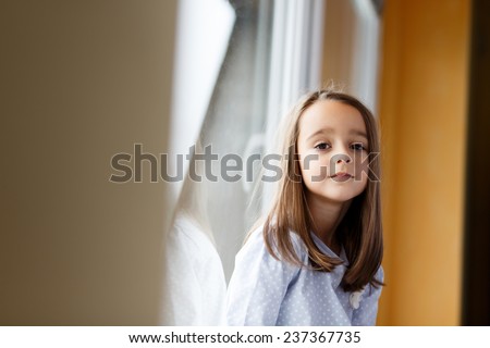 Sad Beautiful little girl watching out the window. A child looks out the window. Young girl looking from window. Portrait of sad kid sits at windowsill.