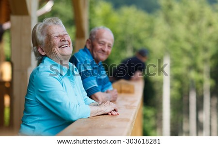 Happy senior couple looking to surroundings areas and smiling. Posing in wooden tower and watching for nature scenery in forest. Summer holidays. Blurred forest background.