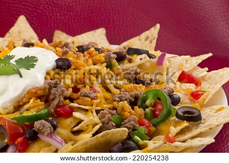 Mexican nachos with sour cream, black olives, ground beef, black beans, tomatoes, shredded cheese, jalapenos, rice, and cilantro
