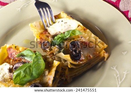 Vegan or vegetarian lasagna dinner topped with mushrooms, olives, artichoke hearts, and fresh basil