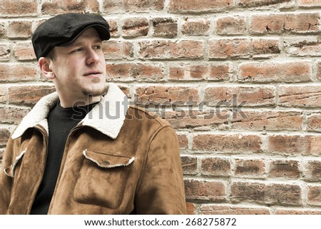 Cool guy rocks an aviator jacket and newsboy cap as he takes a moment to think