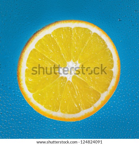 Slice of orange with drop on blue square background
