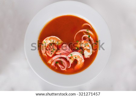 Tomato soup with seafood, prawns, king prawns, octopus, salmon on top of a plate isolated white background for menu