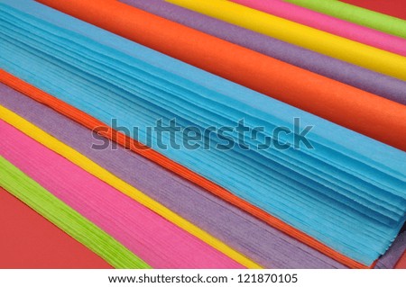 Bright rainbow colored reams (rolls) of tissue wrapping paper on a red background.