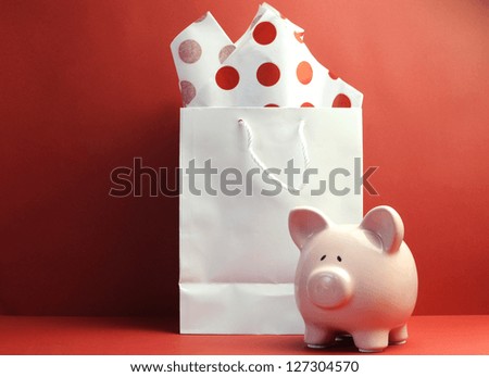 Savings concept with white shopping bag, red polka dot tissue paper, and cute pink piggy bank against a red background.