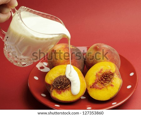 \'Peaches and Cream Complexion\' concept with pouring cream onto a plate of fresh yellow peaches, against a red background.