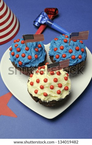 Fourth 4th of July party celebration with red, white and blue chocolate cupcakes on white heart plate and USA American flags with party table setting decorations. Vertical.