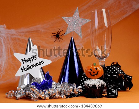 Happy Halloween party decorations with cobweb and spider, champagne glass, hats, chocolate cupcake, stars and streamers on orange background.
