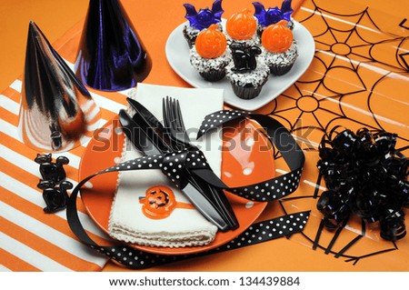 Happy Halloween party table with orange polka dot plates an chocolate cupcakes with black cat, pumpkin and bats decorations on orange background.