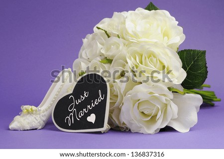 Wedding bouquet of white roses with good luck high heel shoe and heart sign with Just Married message, against purple lilac background.