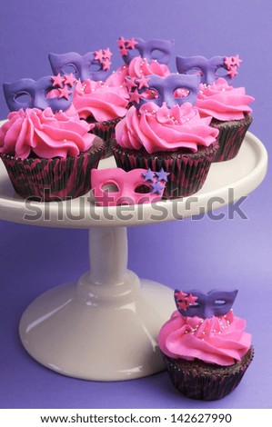 Pink and purple masquerade masks decorated party cupcakes with pink frosting for teenage, birthday, New Years Eve, or wedding bridal shower party - vertical.