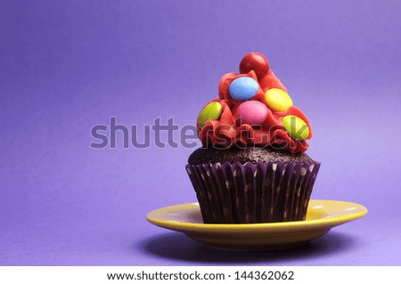 Bright candy covered cupcake on yellow polka dot plate against a purple background for Children\'s Birthday, Halloween trick or treat, or Christmas party.