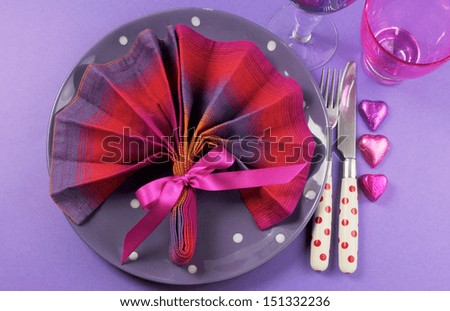 Pink and purple table setting with fan shape napkin setting and polka dot plate and cutlery with heart shape chocolates and pink & purple glasses for fun birthday or special occasion dining table.