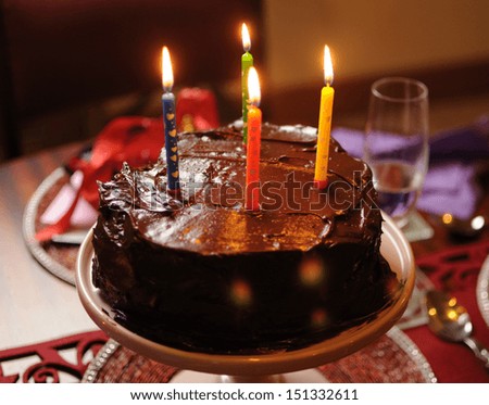 Happy birthday heart shape chocolate mud cake with four lit birthday candles on party party table setting.