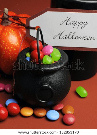 Halloween Trick or Treat witches cauldrons full of candy on autumn brown background with black candle and orange pumpkin. Close up.