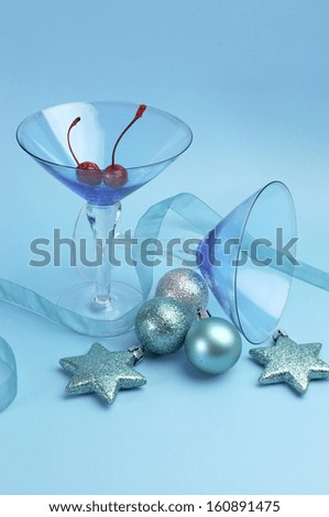 Festive spirit blue martini cocktail glasses with red maraschino cherries and christmas baubles on an aqua blue background. Vertical.