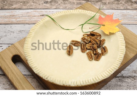 Holiday festive baking with an empty pie shell pastry crust with raw pecan nuts ingredients and autumn leaf decoration.