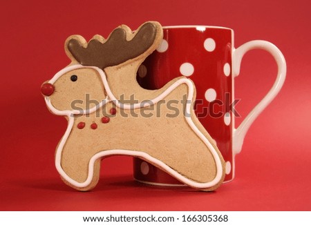 Reindeer vanilla cookie biscuit with red polka dot cup of coffee against a festive red background for happy holidays or merry Christmas cheer.
