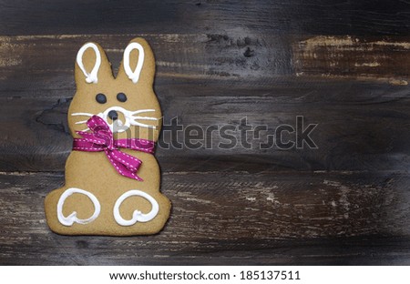 Happy Easter bunny rabbit gingerbread cookie with pink ribbon on dark recycled vintage retro wood timber background with copy space for your text here.