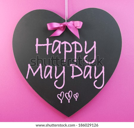 Happy May Day handwriting greeting on heart shaped blackboard for 1st First of May celebrations on pink background.