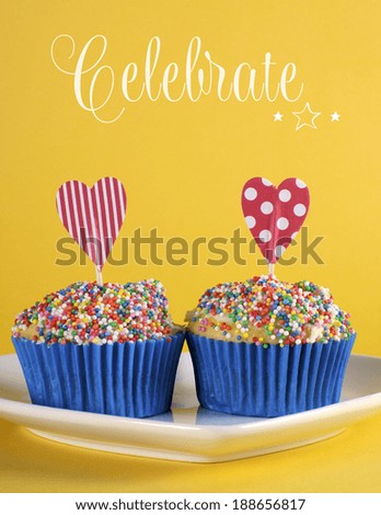 Bright and cheery red blue and yellow theme cupcakes with hundred and thousands candy topping and heart toppers for birthday or special occasion with sample Celebrate text or copy space.