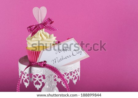 Happy Mothers Day pink heart cupcake on white cupcake stand with greeting gift tag against a feminine pink background, with copy space for your text here..