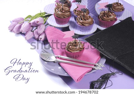 Graduation day pink and purple party table setting with chocolate cupcakes, purple polka dot cupcake stand, graduation cap, tulips and copy space for your text here.