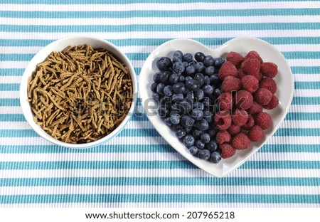 Healthy diet high dietary fiber breakfast with bowl of bran cereal and berries on white heart plate on aqua blue and white place mat.