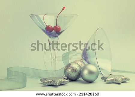 Festive spirit blue martini cocktail glasses with red maraschino cherries and christmas baubles on an aqua blue background. Vertical with retro vintage filter.