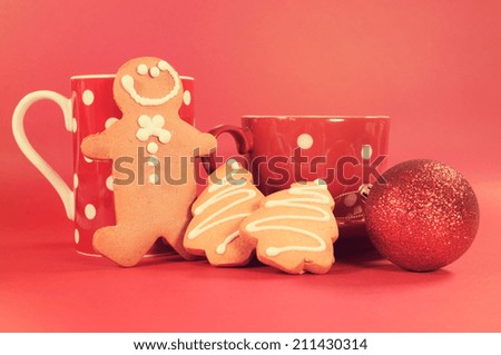 Gingerbread man with red polka dot coffee mug and tea cup with Christmas tree shape cookies against a red background. with retro vintage filter.