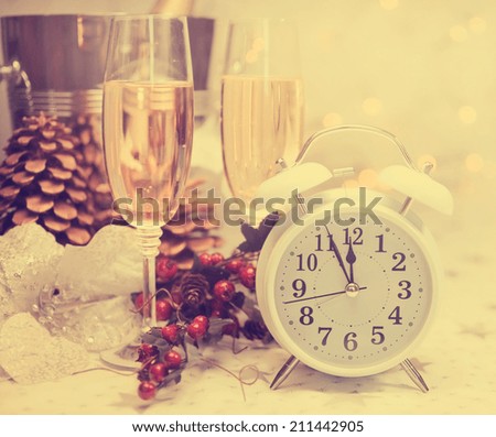 Happy New Year table setting with white retro clock showing five to midnight with champagne and festive decorations against white starry background with bokeh lights, with retro vintage filter.