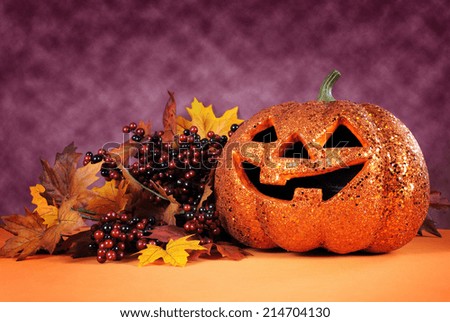 Happy Halloween orange glitter jack-o-lantern pumpkin with autumn leaves and berries against a bright modern colorful dark pink and orange background.