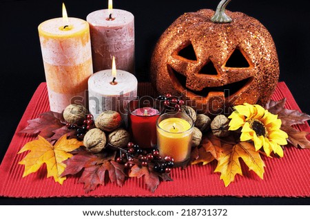 Happy Halloween party table centerpiece with orange glitter jack-o-lantern pumpkin with lit candles and autumn Fall leaves, nuts and berries on black tablecloth.