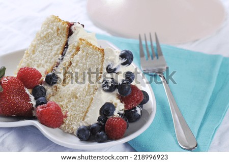 Slice of fresh whipped cream and berries layer sponge cake with fork and pale blue napkin.