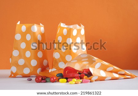 Row of Happy Halloween orange polka dot trick or treat paper bags with multi-color candy against and orange and white background.