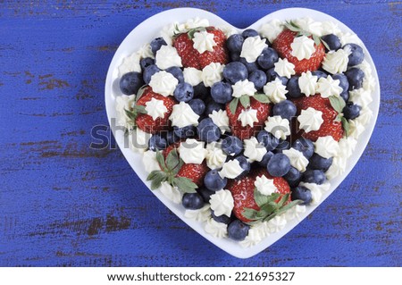 Patriotic red, white and blue berries with fresh whipped cream stars in white heart shape flag on rustic dark blue wood background, with copy space.