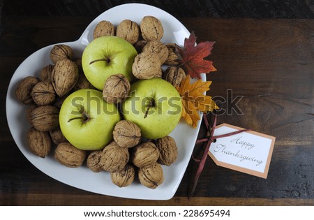 Happy Thanksgiving Autumn Fall harvest fruits with green apples and walnut nuts in white heart shape plate on dark recycled wood background, with copy space, with gift tag.