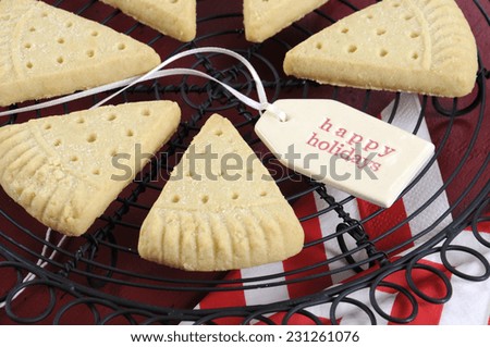 Christmas shortbread triangle cookies on vintage baking rack on dark red rustic wood background with festive decorations. Closeup.