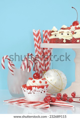 Christmas holiday dessert party food with cherry cupcakes and Santa strawberries in modern red and white trend against pale blue and white background. Vertical.