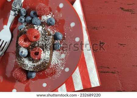 Christmas holiday chocolate roulade swiss roll with berries dessert party food on red polka dot plate on red wood table.