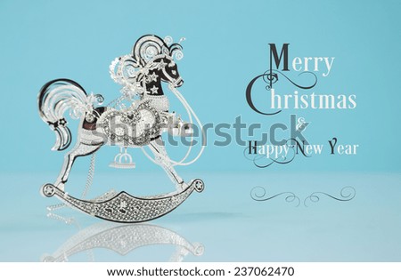 Beautiful vintage silver rocking horse ornament on pale blue and white background with Merry Christmas and Happy New Year greeting text.